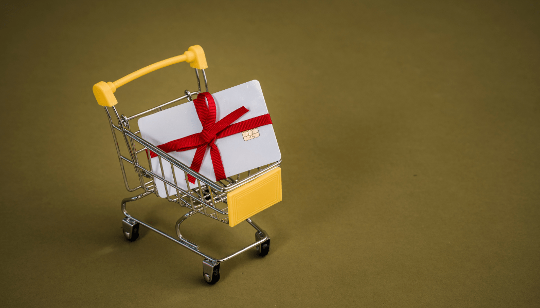 Gift card with red ribbon in small shopping cart on brown background